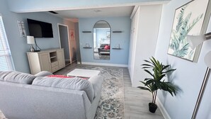 Een moderne woonkamer met een grijze bank, een klein wit tafeltje en een potplant.