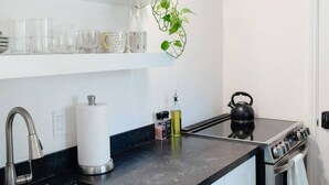 A modern kitchen with white cabinetry, a black countertop, a stainless steel sink, and a kettle. - Montecito Orchard Cottage (Montecito)