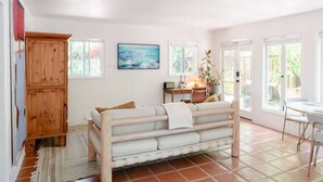 A cozy room with a wooden bed, a desk, and a chair. There is a window with a view of greenery outside. - Montecito Orchard Cottage (Montecito)