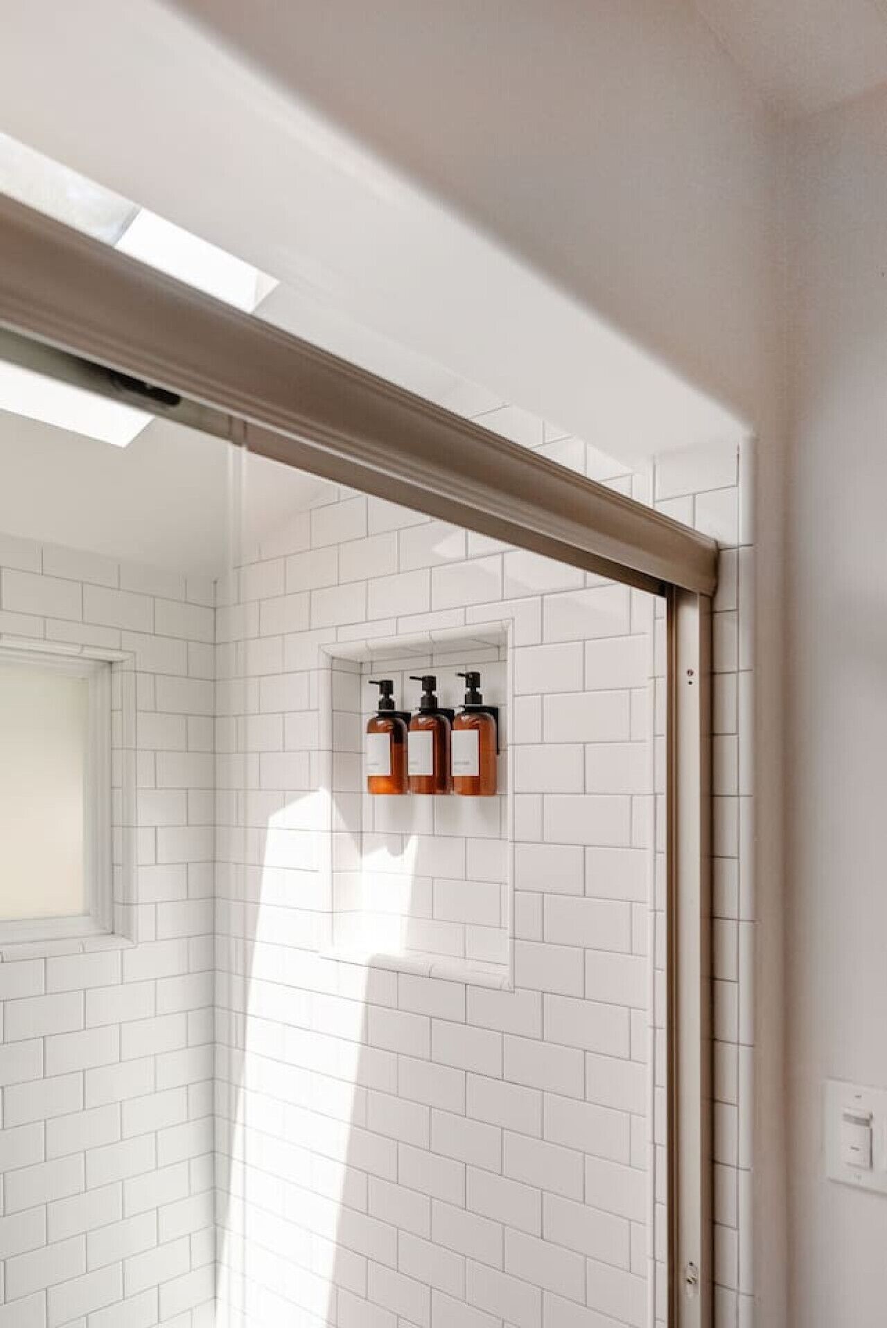 A bathroom with white subway tiles, a glass shower enclosure, and three soap dispensers mounted on the wall.