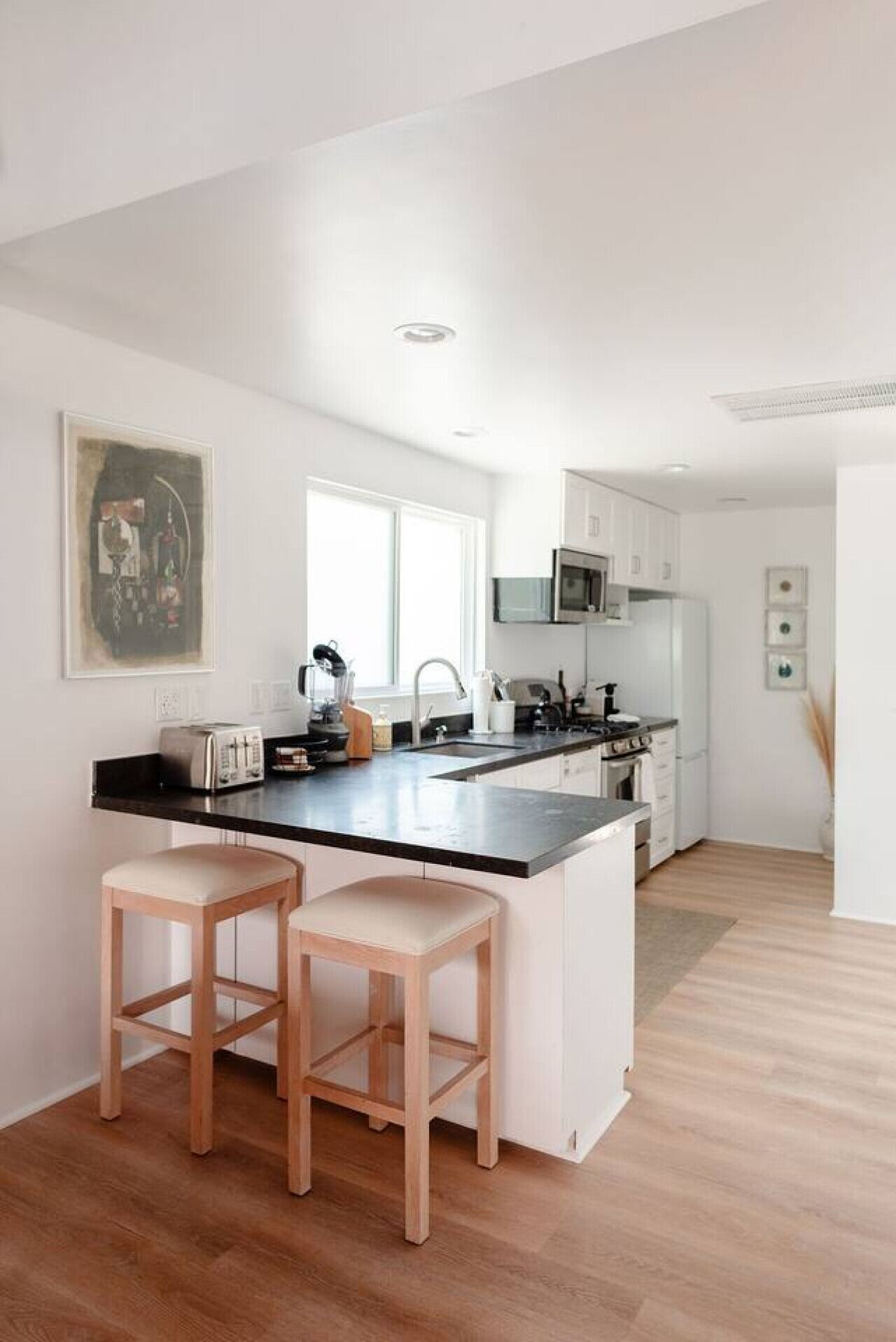 A modern kitchen with a central island, bar stools, and a microwave.