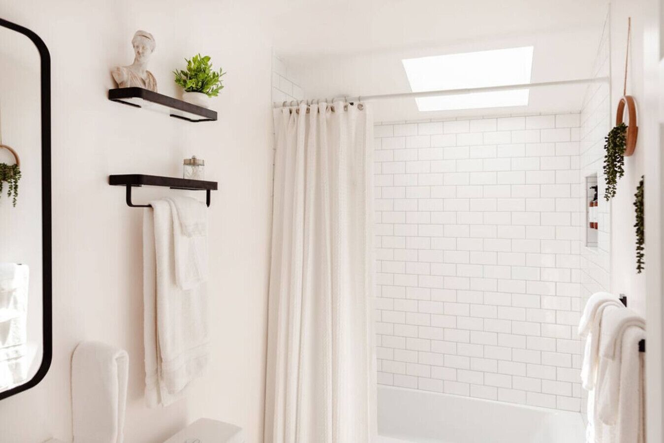 A modern bathroom with white brick walls, a skylight, a shower with a curtain, and a mirror with a plant on the wall.