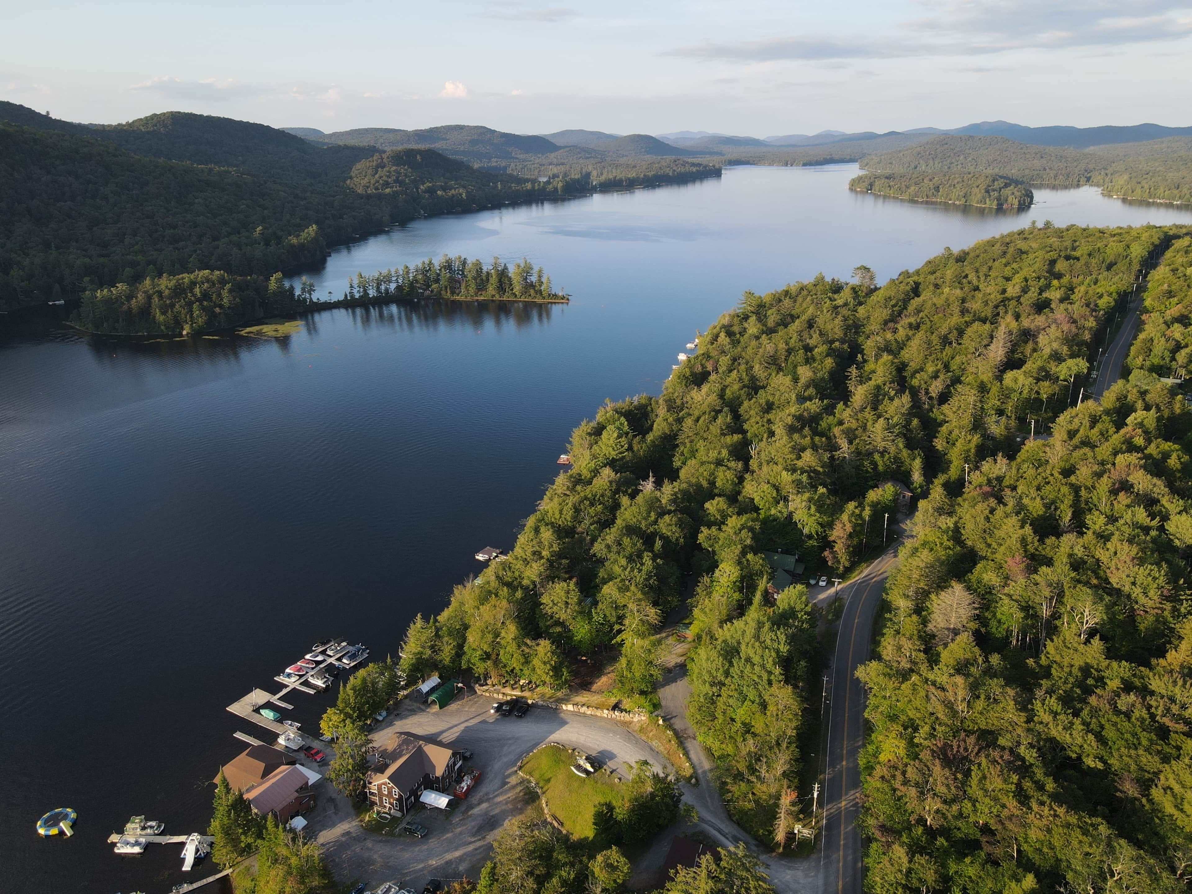 Vue aérienne d’une propriété au bord du lac, avec un quai, un petit bâtiment et une route menant à celle-ci.