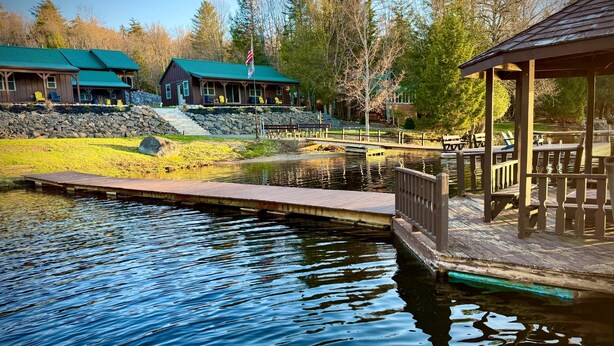 A lakeside lodge with a dock, a covered seating area, and a stone wall. - Fern - Big Moose Lakeside (Eagle Bay)