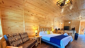 A wooden cabin interior with a bed, sofa, and a small kitchenette. - Fern - Big Moose Lakeside (Eagle Bay)