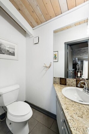 A bathroom with a white toilet, a sink with a granite countertop, and a wooden ceiling. - Snow Summit Cabin Big Bear- 25ft to Snow Summit! (Big Bear Lake)