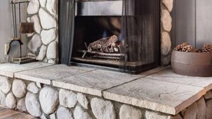 A stone fireplace with a built-in bench, a mantel shelf with decorative items, and a log fire. - Snow Summit Cabin Big Bear- 25ft to Snow Summit! (Big Bear Lake)