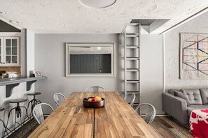 A dining area with a wooden table, chairs, a fruit bowl, a ladder, and a sofa. - Snow Summit Cabin Big Bear- 25ft to Snow Summit! (Big Bear Lake)