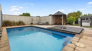 A rectangular swimming pool with a tiled deck, a small covered seating area, and a fenced backyard. - Bayfair Break - Mt Maunganui (Mt Maunganui)
