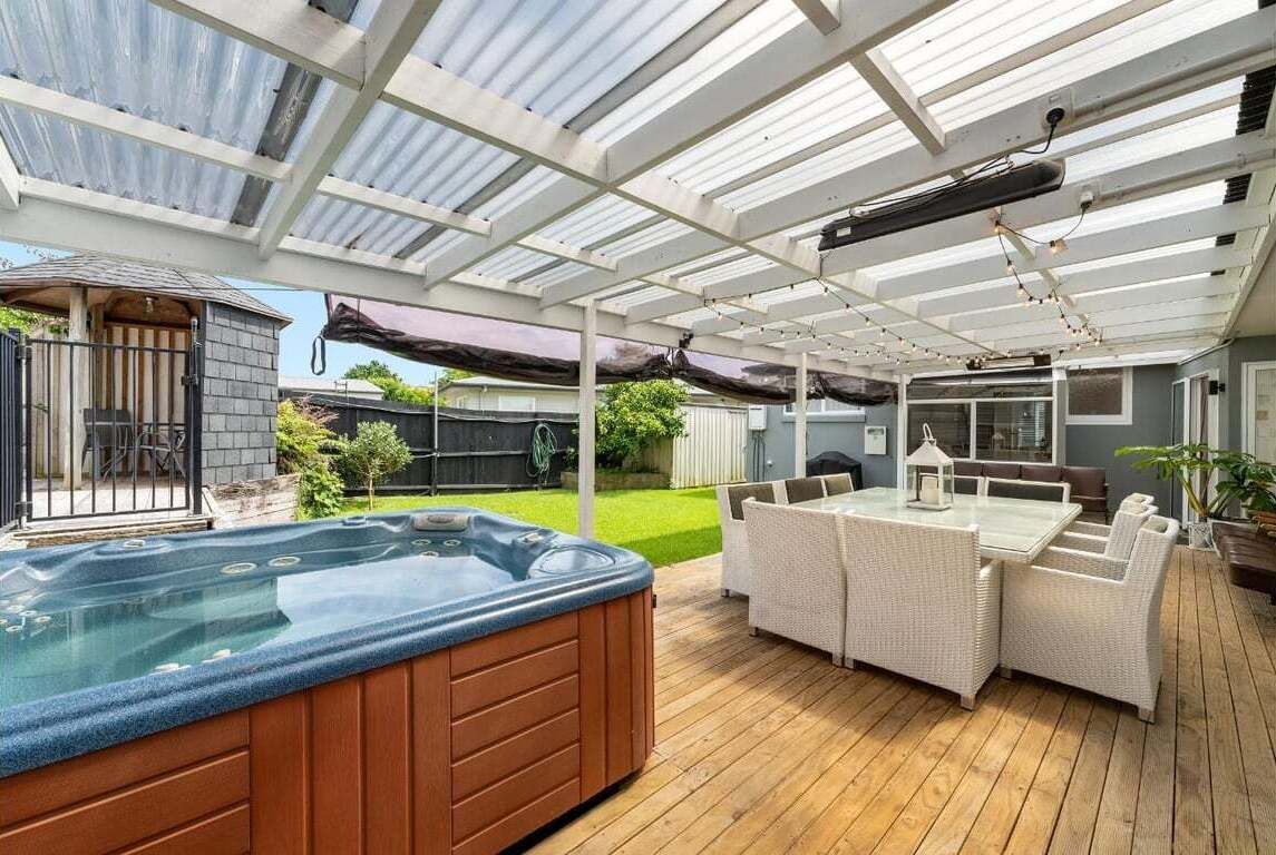Une terrasse couverte avec un jacuzzi, du mobilier d’extérieur et une vue sur le jardin.