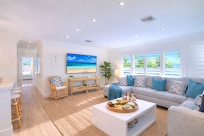A spacious living room with a large TV, a sofa, a coffee table with snacks, and a view of the outdoors. - Las Olas Oasis: Heated Pool, Hot Tub, Near Beach (Fort Lauderdale)