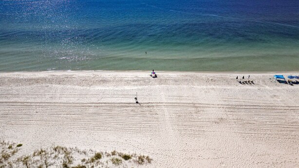 A beach with clear skies, calm water, and a few people and umbrellas. - New! Steps to Beach & Lagoon~Pool~Family Fun~Paddle Boards (Gulf Shores)