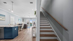 A modern kitchen with a blue island, wooden staircase, and a dining area with a view of the beach. - New! Steps to Beach & Lagoon~Pool~Family Fun~Paddle Boards (Gulf Shores)