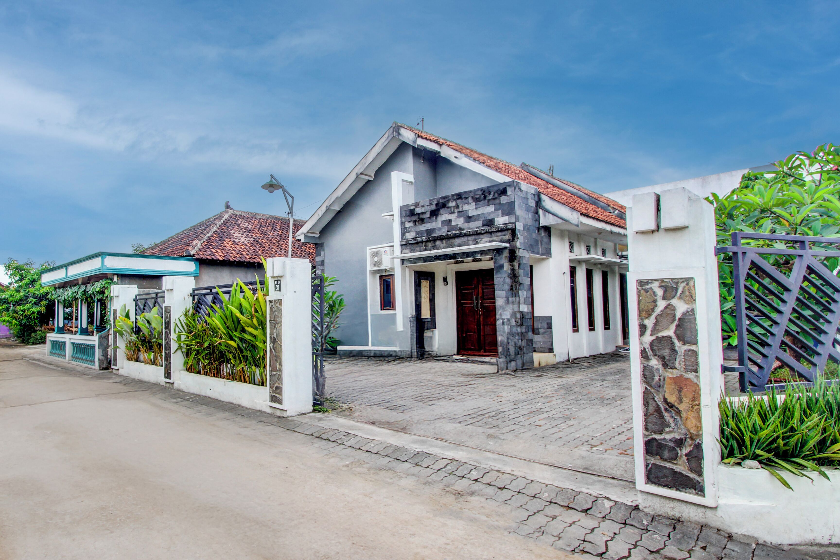 A two-story house with a tiled roof, a stone pillar, and a gated entrance.