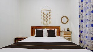 Een net opgemaakt bed met een houten hoofdbord, een nachtkastje met een lamp, en een decoratief object aan de muur.