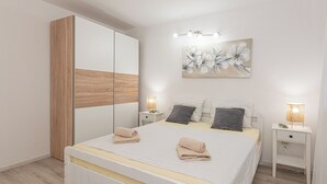 A modern bedroom with a large bed, a wardrobe, bedside lamps, and a floral artwork on the wall. - 4-bedroom villa in beautiful Ljubotić with AC, Rural Villa Olive Krka (Ljubotić)