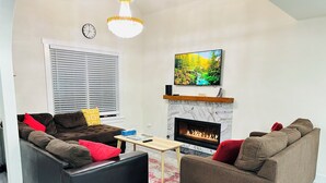 Una sala de estar con chimenea, dos sofás, una mesa de centro y un televisor sobre la chimenea.