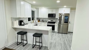 Cocina moderna con armarios blancos, electrodomésticos de acero inoxidable y una isla central con dos taburetes.