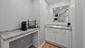 Un baño moderno con encimera de granito, cafetera, lavamanos y espejo.