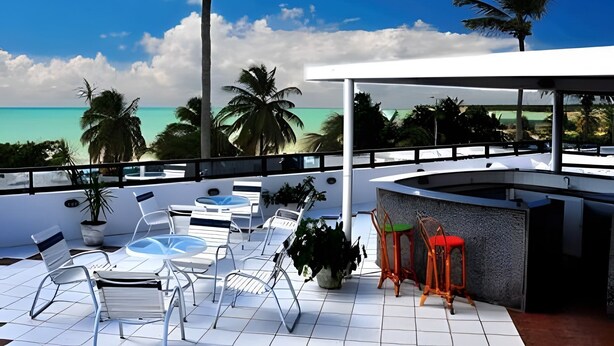 A rooftop terrace with white tiled flooring, outdoor seating, and a view of the ocean and palm trees. - 119 Ambassador  (Joao Pessoa)