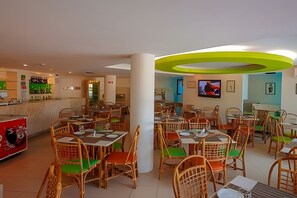 Un restaurante con varias mesas y sillas, una zona de bar y una pantalla de televisión.