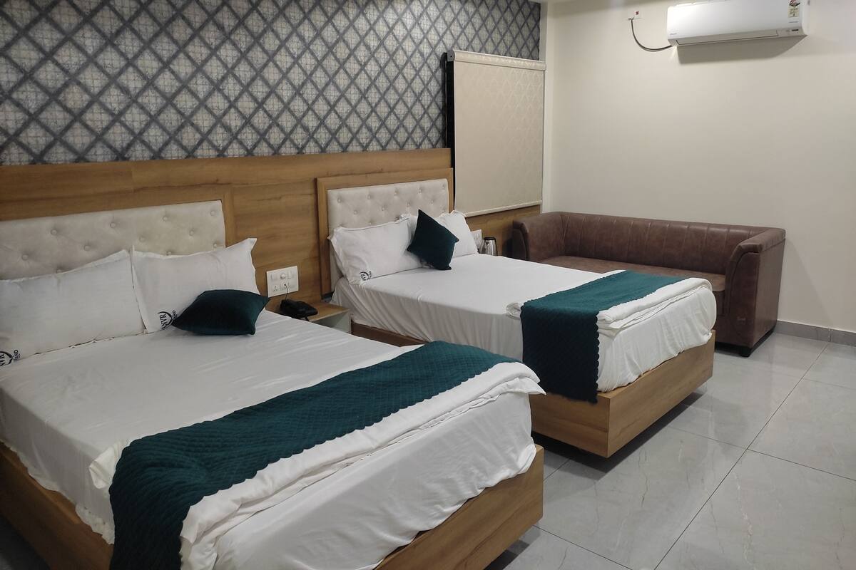 Habitación de hotel con dos camas, un sofá marrón, un ventilador de techo y un equipo de aire acondicionado.
