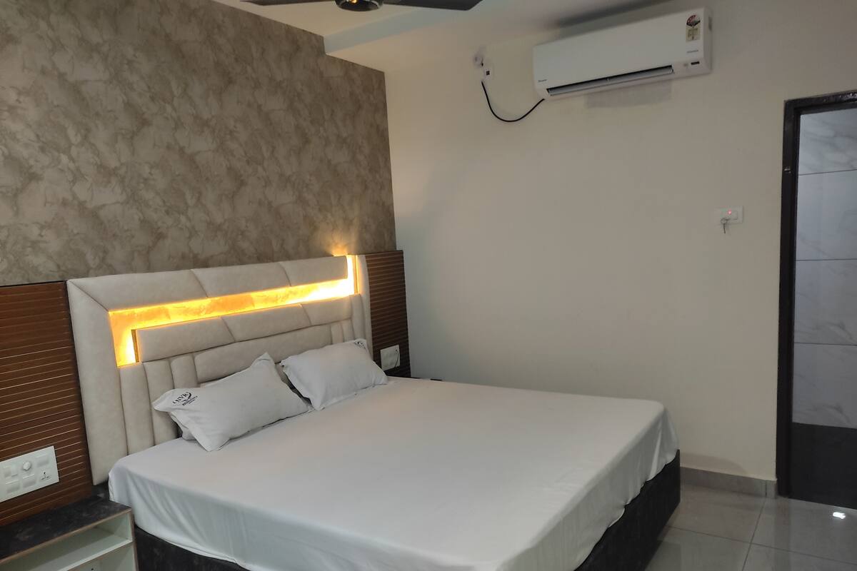 Una habitación de hotel moderna con una cama grande, un cabecero con iluminación integrada, una mesita de noche y un equipo de aire acondicionado instalado en la pared.