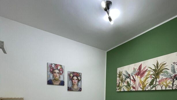 A bedroom with a bed, a wooden shelf, two paintings, and a green accent wall. - Sicilia Bedda Vacation Rental (Lascari)