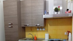 A compact kitchen with wooden cabinets, a sink, and a small dining area with a round table and two chairs. - Sicilia Bedda Vacation Rental (Lascari)
