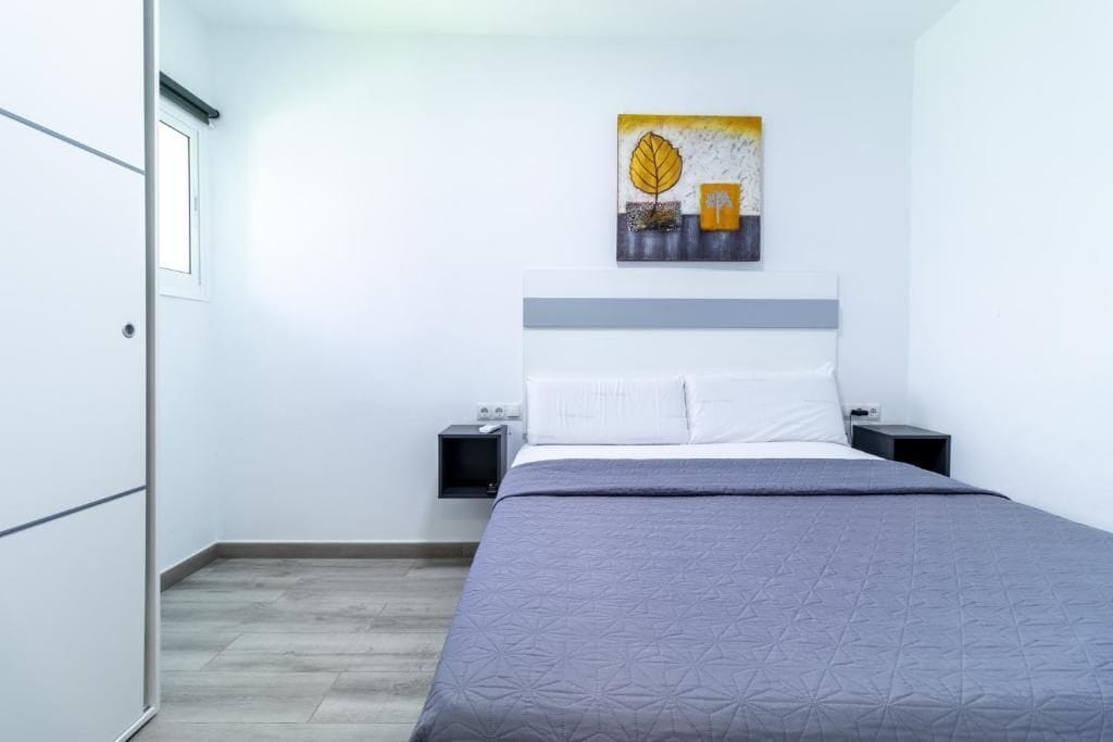 A bedroom with a bed, a nightstand, a wall-mounted painting, and a door.