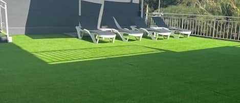 A pool area with artificial grass, lounge chairs, and umbrellas.