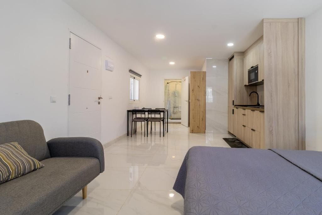 Une pièce moderne comprenant un canapé, une table à manger avec des chaises, un coin cuisine et une porte donnant sur une autre pièce.