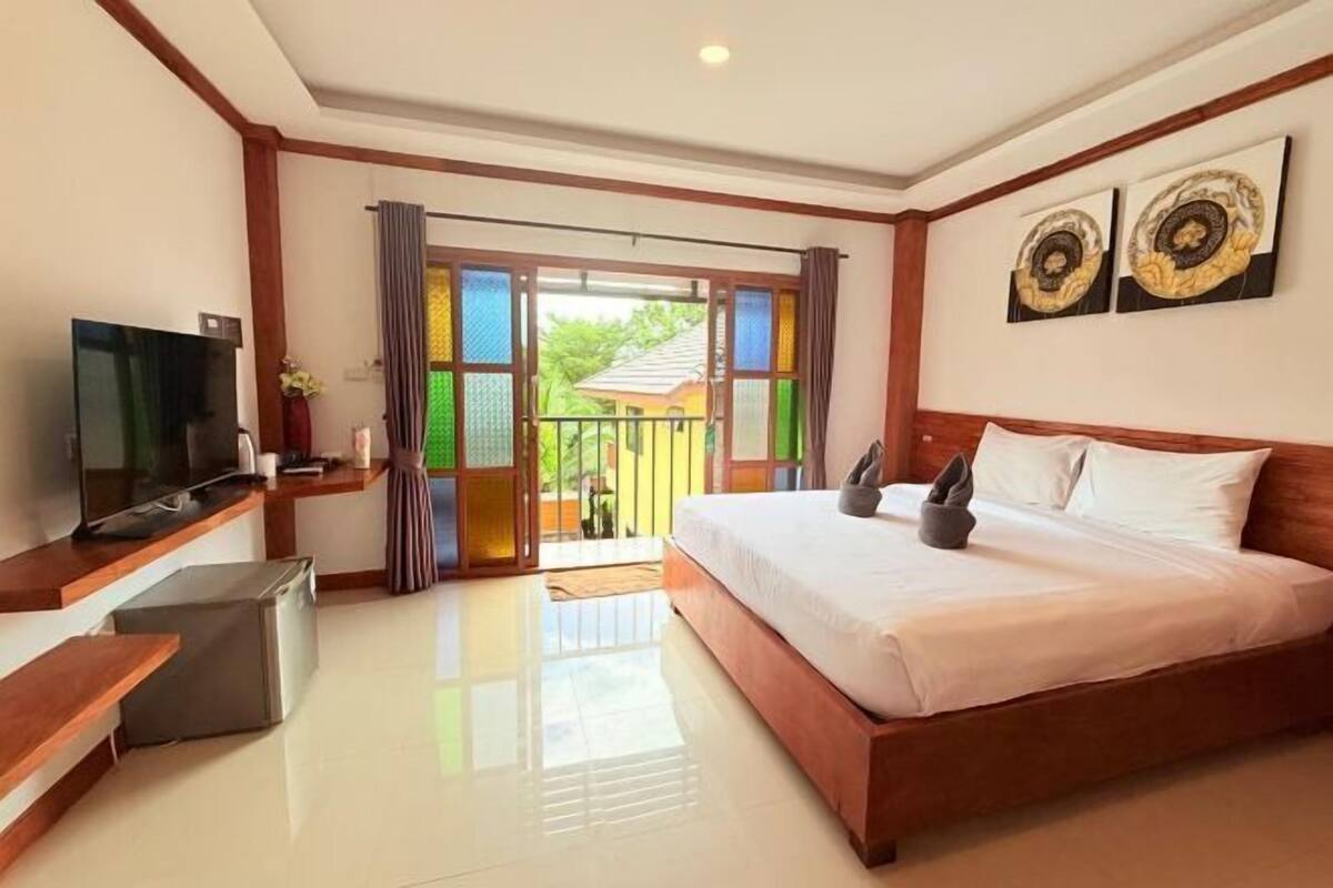A bedroom with a bed, a TV, a small fridge, and a balcony with colorful glass doors.