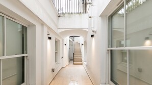 A corridor with large windows on both sides, leading to a staircase. - Chic Pimlico Escape with Style & Comfort (London)