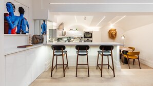 A modern kitchen with a central island, bar stools, and a dining area with a table and chairs. - Chic Pimlico Escape with Style & Comfort (London)