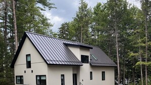 A modern two-story house with a sloped roof, surrounded by a natural forest setting. - Modern Lakehouse on Quiet Peninsula (Lakeville)