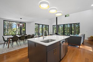 A modern kitchen with a central island, large windows, and a dining area with chairs.