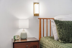 A neatly made bed with a green quilt, a bedside lamp, and a small green alarm clock on a wooden nightstand. - Modern Lakehouse on Quiet Peninsula (Lakeville)