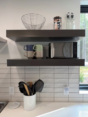 A kitchen with a microwave, two mugs, a metal strainer, and a white mug with utensils. - Modern Lakehouse on Quiet Peninsula (Lakeville)