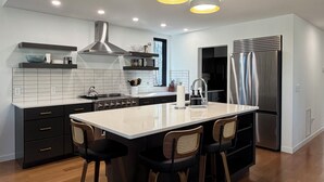A modern kitchen with a central island, bar stools, and a stainless steel refrigerator. - Modern Lakehouse on Quiet Peninsula (Lakeville)
