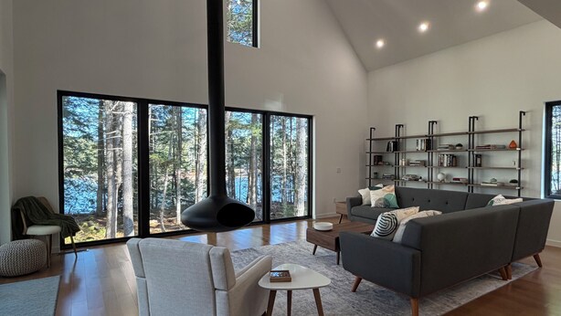 A spacious living room with a large fireplace, a grey sofa, a white armchair, and a bookshelf. - Modern Lakehouse on Quiet Peninsula (Lakeville)