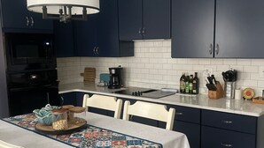 Una cucina moderna con mobili blu scuro, un piano di lavoro bianco e un tavolo da pranzo con una tovaglia colorata.