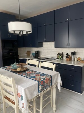 A modern kitchen with dark blue cabinets, a white countertop, and a dining table with a colorful tablecloth. - Charming historic home close to the World Cup (Atlanta)