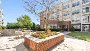 A courtyard with a brick planter, outdoor seating, and a building with multiple windows and balconies. - Landing Apartments New York  (Raritan)