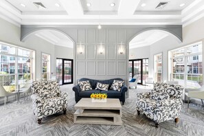 A spacious lobby with a dark blue sofa, patterned armchairs, and a coffee table with sunflowers. - Landing Apartments New York  (Raritan)