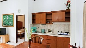 A compact kitchen with wooden cabinets, a dining table, a TV, and a painting on the wall. - Rumah Akira Seminyak (Bali)