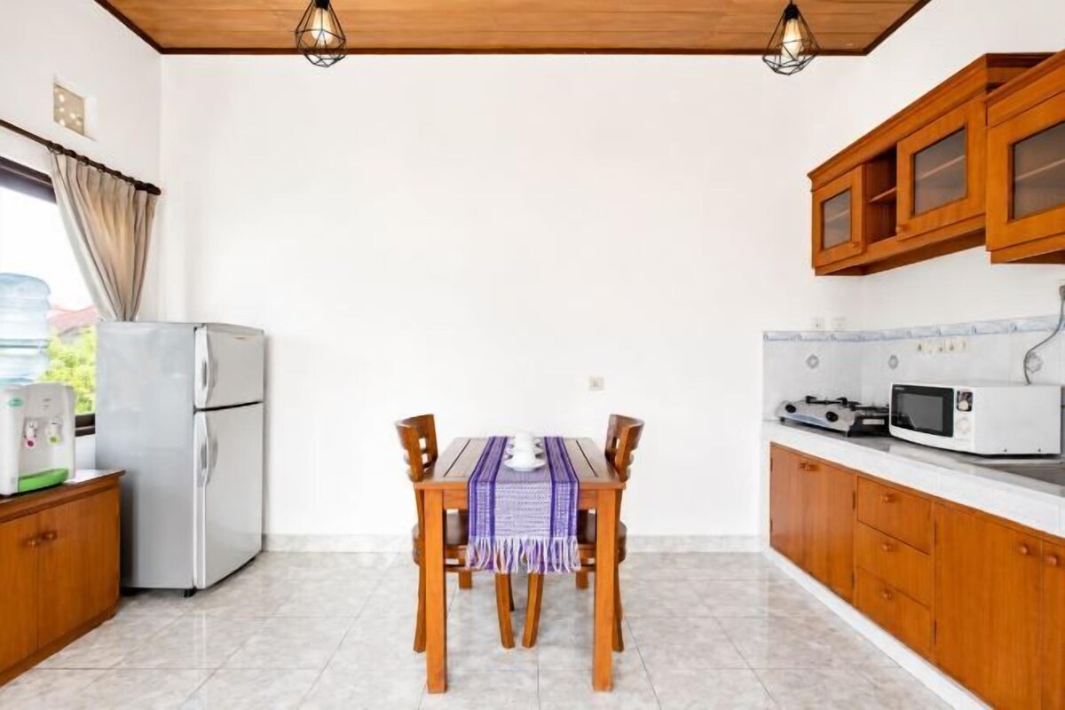 A kitchen with a dining table, wooden cabinets, a refrigerator, and a microwave.
