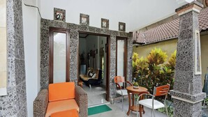 A room with a stone wall, a wicker sofa, a wooden table, and chairs. - Rumah Akira Seminyak (Bali)
