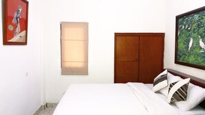 A bedroom with a bed, a wooden wardrobe, a window with blinds, and two framed pictures on the wall. - Rumah Akira Seminyak (Bali)