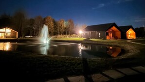 A nighttime scene with a lit fountain, a building with a dark roof, and a lit-up house. - The Cork Cottages, Unit 1, Arcade Table, Modern and New 2b/2b (Geneva)